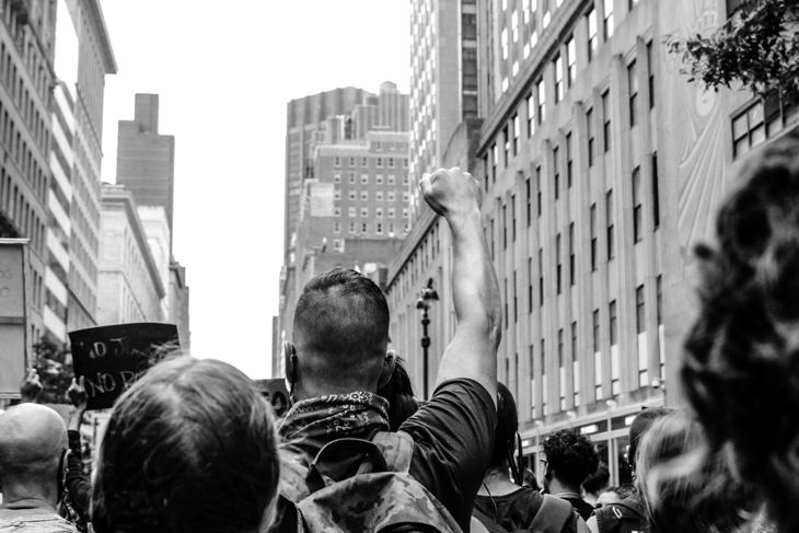 Black and white photo capturing individuals protesting on an urban road.